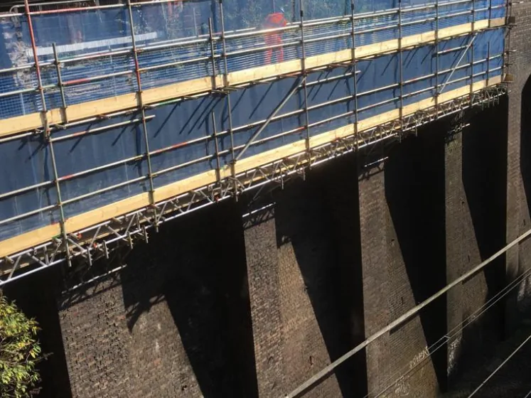 Cantilevered scaffold needled over a viaduct parapet, with the working platform hanging below the top edge