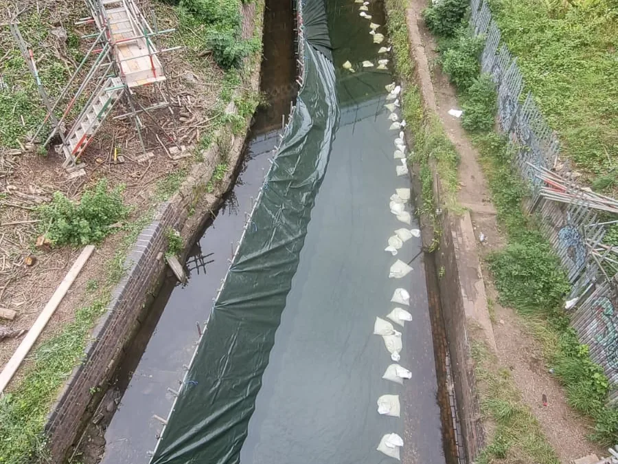 Scaffold cofferdam in a live river channel with a vinyl membrane and gravel bag ballast holding back the flow