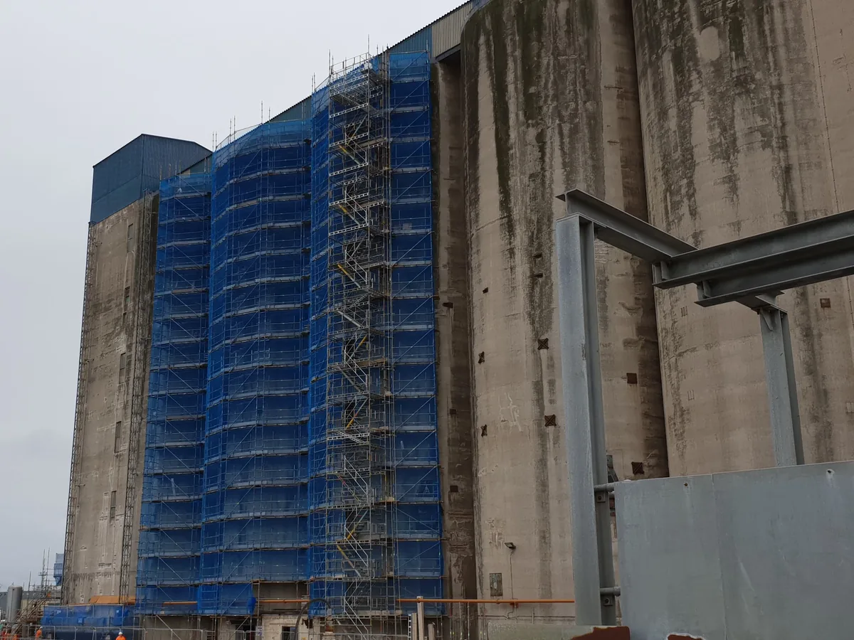 Tall netted independent scaffold on the face of dockside concrete silos