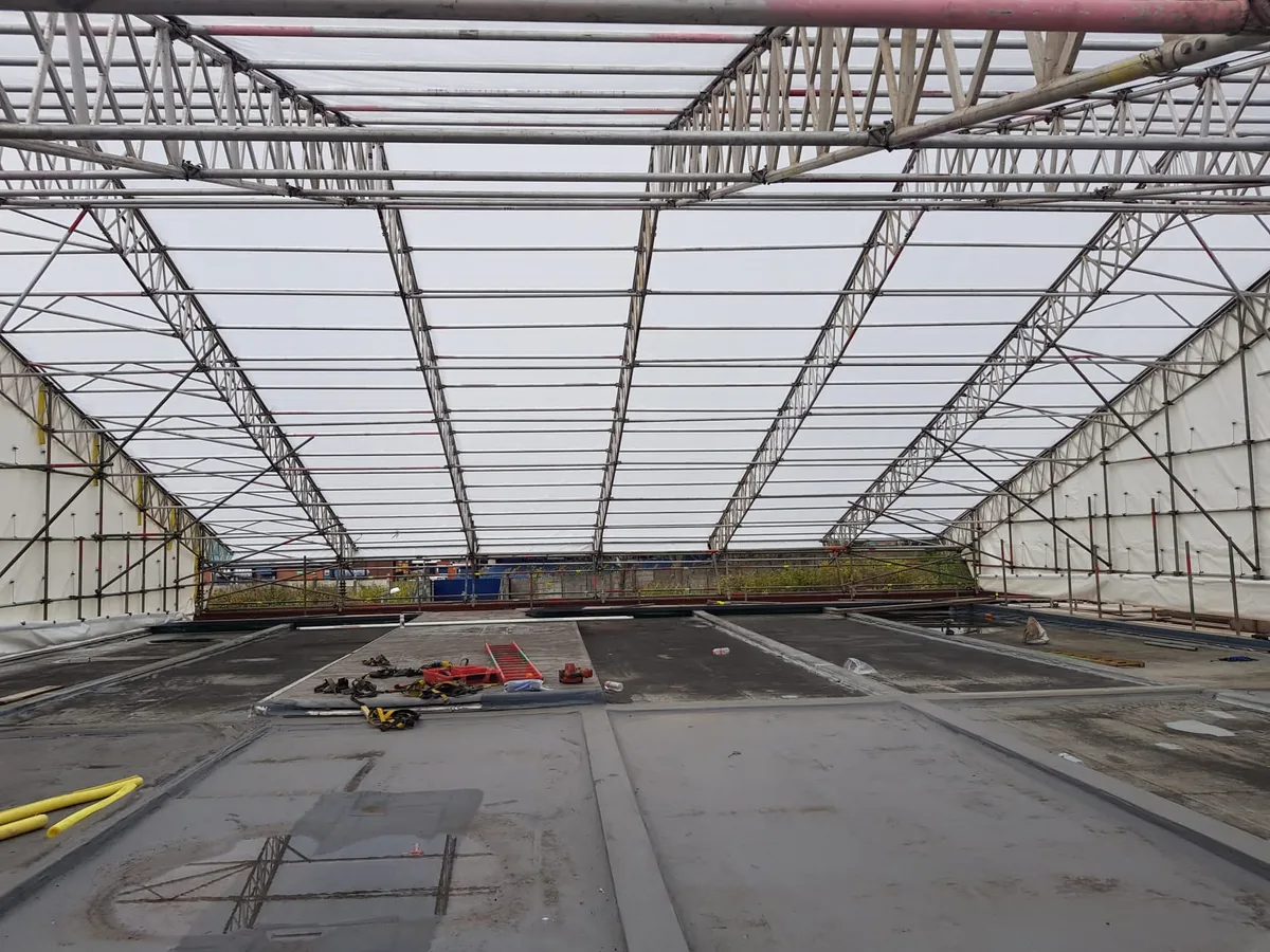 Inside a temporary roof: lattice beams and translucent sheeting spanning a flat roof